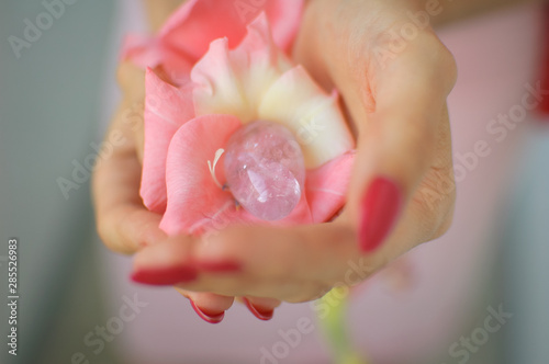 Close up photo of female hand with transparent amethyst yoni egg for vumbuilding inside pink gladiolus flower. Top view of quartz crystal in hands. Womens health concept