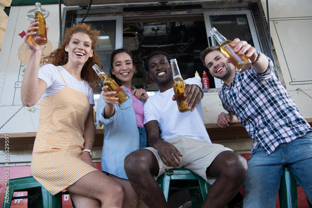 low angle view of happy multicultural friends holding bottles with beer near food truck