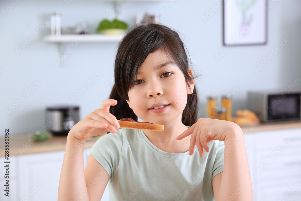 Funny little girl eating tasty toast with jam in kitchen Funny little girl eating tasty toast with jam in kitchen