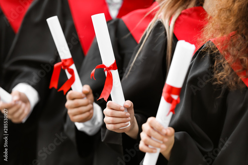 Young students in bachelor robes and with diplomas outdoors