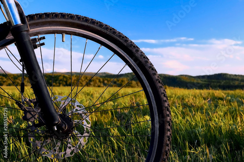 Close-up of a bicycle wheel in a summer meadow against the sky and mountains