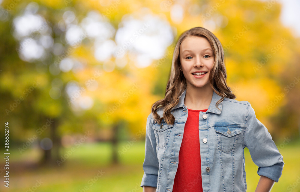 people concept - smiling teenage girl with long hair in denim jacket over autumn park background people concept - smiling teenage girl with long hair in denim jacket over autumn park background