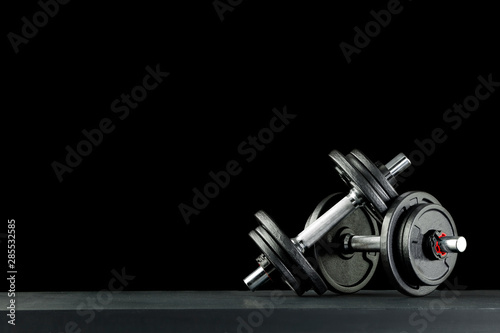 A woman and workout in the gym. Barbell, dumbbell held in hand on black background. photo
