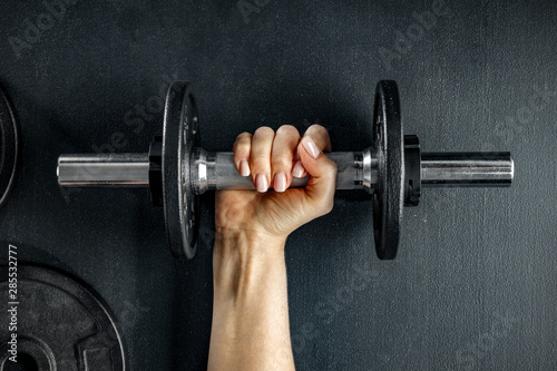 A woman and workout in the gym. Barbell, dumbbell held in hand on black background.