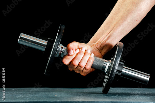 A woman and workout in the gym. Barbell, dumbbell held in hand on black background.