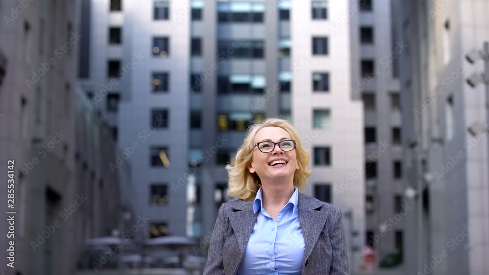 Happy blond woman in formal suit standing outside business center, work progress Happy blond woman in formal suit standing outside business center, work progress