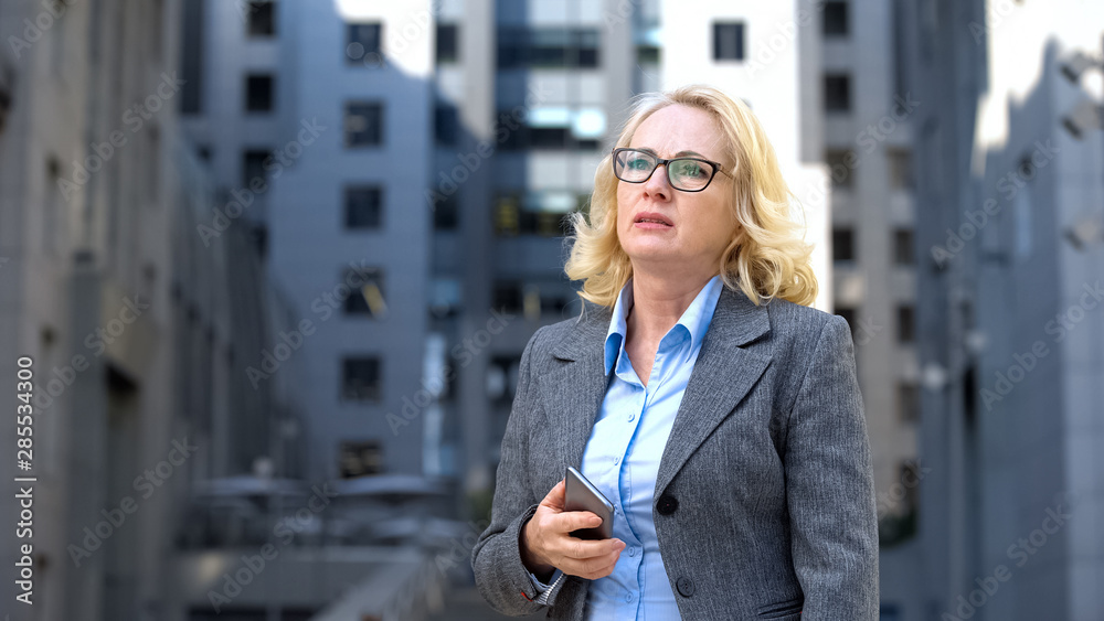 Fototapeta premium Worried company manager holding smartphone thinking of work problem outdoors