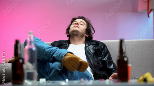Photography Intoxicated young man relaxing on sofa, alcohol bottles on table, students party