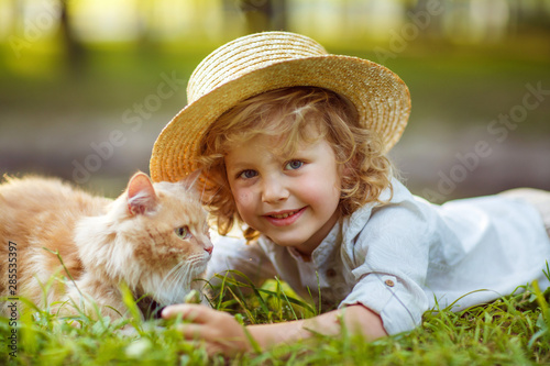 Little curly boy with a redhead cat, outdoor summer day