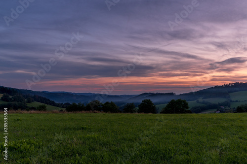 Morning sunrise in Beskyd area colored dark sky with clouds and fresh fog covering grass around mountains and hills behind in the valley.