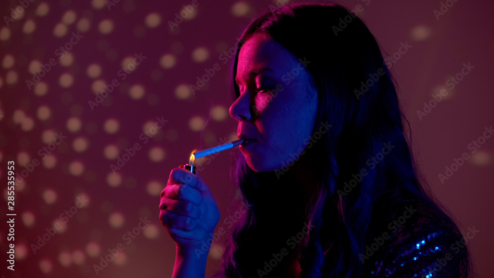 Fototapeta premium Woman lighting cigarette in night club, harmful addiction, lungs cancer risk