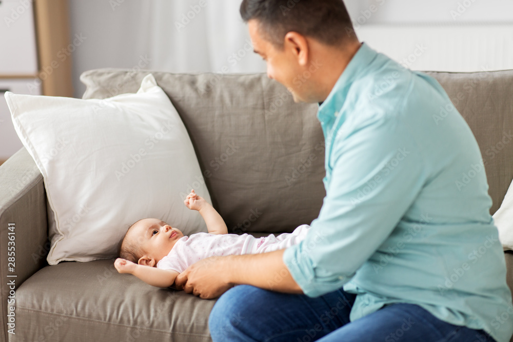 family, parenthood and fatherhood concept - middle aged father playing with little baby daughter lying on sofa at home family, parenthood and fatherhood concept - middle aged father playing with little baby daughter lying on sofa at home