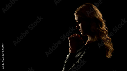 Blond woman praying in dark place, asking for forgiveness, sinner confession