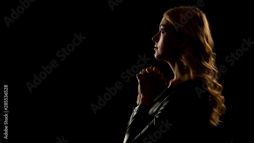Female sinner praying looking up, isolated on black background, confession