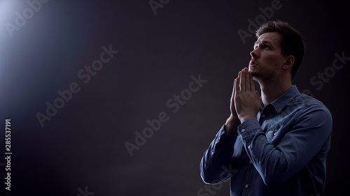 Foto Young man praying in dark room under blessed light from heaven, Christianity