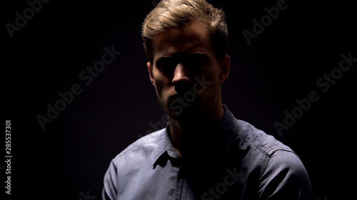 Shy shadowed man looking at camera on black background  mens health  criminal