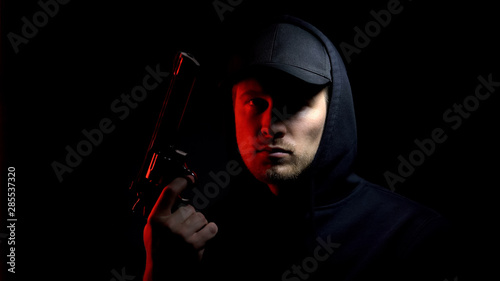 Tableau sur toile Male hooligan with gun against dark background, danger criminal ready to robbery