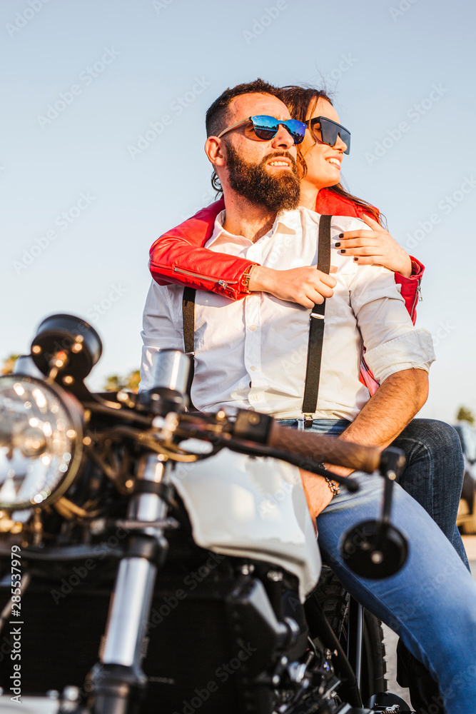 Portrait of couple sitting on motorbike at evening twilight looking at distance