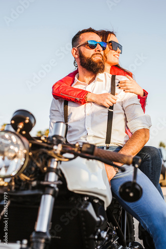 Portrait of couple sitting on motorbike at evening twilight looking at distance