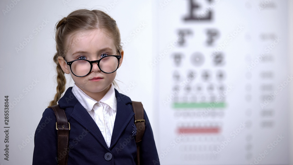 Cute schoolgirl looking over glasses, serious child with good vision, correction Cute schoolgirl looking over glasses, serious child with good vision, correction