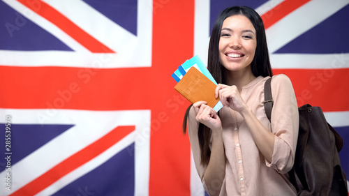 Happy female traveler holding passport with flight tickets against British flag