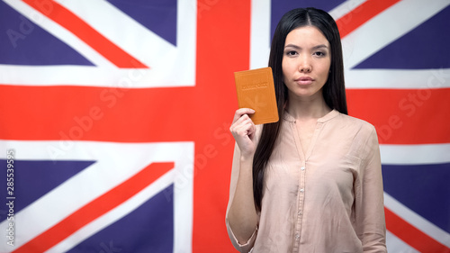 Confident Asian woman showing passport against British flag background, emigrant