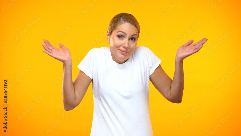 Fototapeta premium Doubtful woman throwing up hands on bright background, having no idea, choice