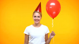 Cheerful lady party horn holding red balloon on bright background, holiday