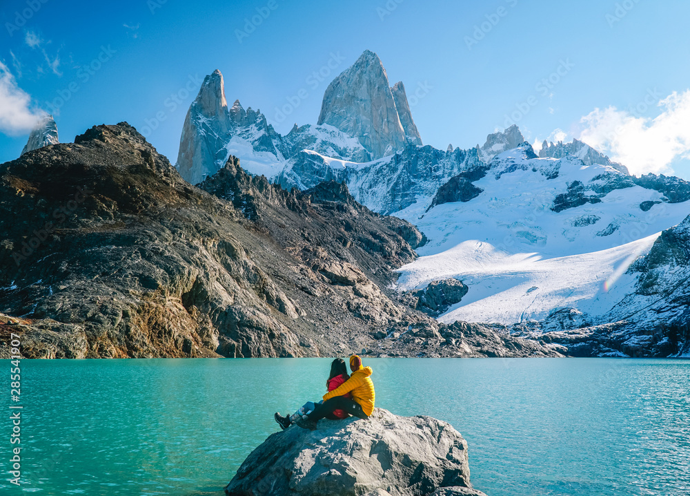 Couple in love at Mount Fitzroy. Scenic view of snowcapped mountain tops of Patagonia trek. Blue sky, turquoise lake and scenic rock landscape. Shot in Argentina. Nature, travel, adventure, hiking. - obrazy, fototapety, plakaty 
