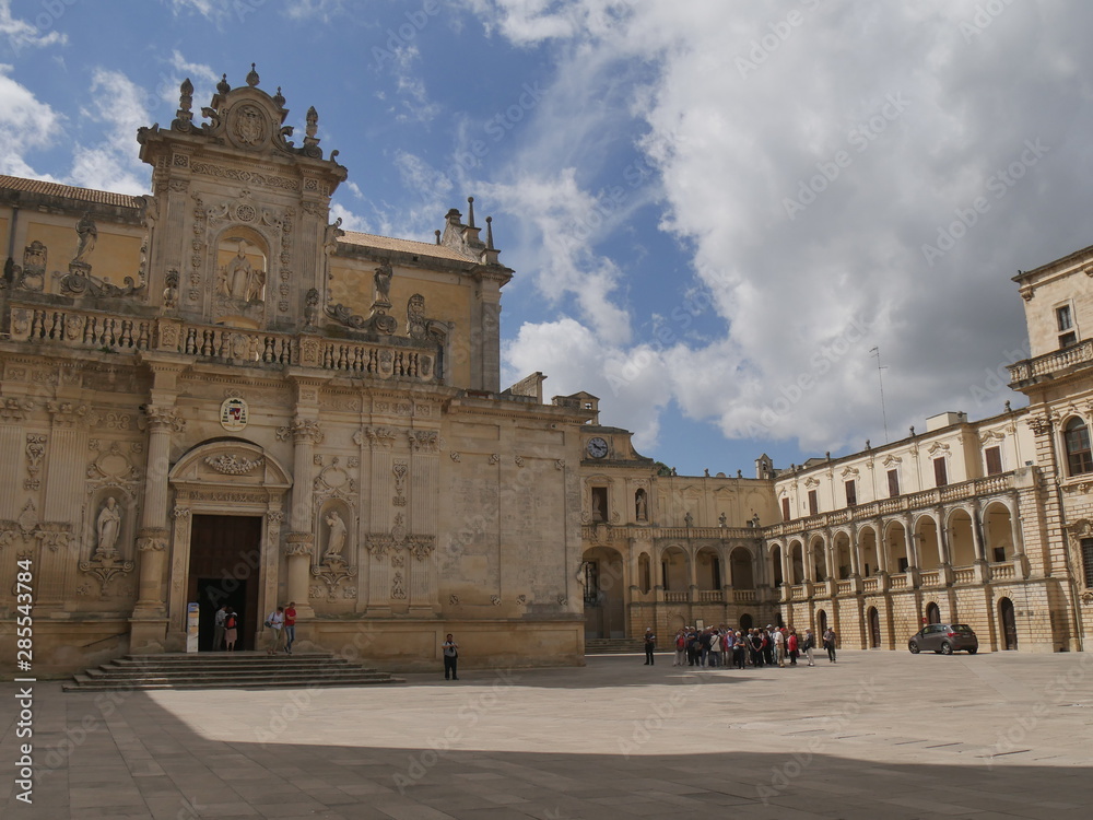 Lecce – Piazza Duomo. It includes : double facade Cathedral dedicated to the Assumption of the Virgin ; Bell Tower ; Seminary with baroque facade ; Bishop monumental palace surmounted by a clock.