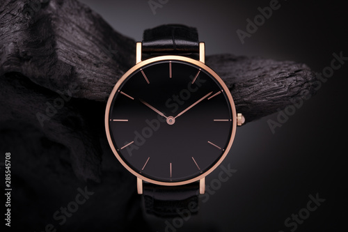 A luxury gold watch with a black dial. A watch on a beautiful stand, on a beautiful lightly lit gray background. Woman/Man fashion photo