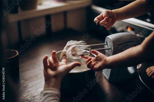 Several small hands fingering whip cream off of the mixer blades.