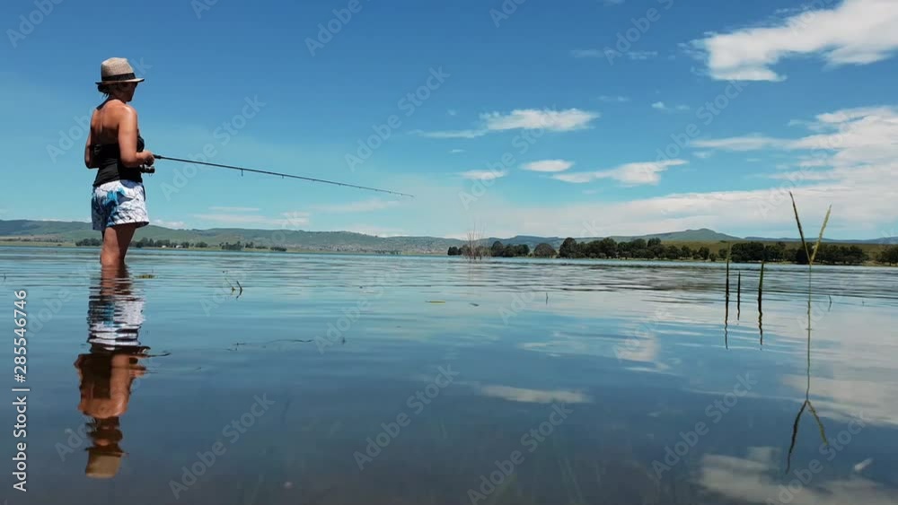 Girl standing in a clear blue lake fishing on a sunny day Girl standing in a clear blue lake fishing on a sunny day
