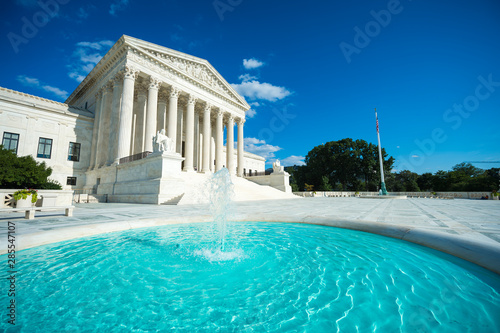 Bright scenic sunny view of the front exterior of the United States Supreme Court building with blue waters of a fountain in the foreground in Washington DC, USA