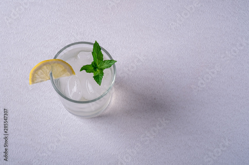 Fresh cold clear water drink in glass with ice cubes, lemon slice and mint leaf, on white gray background
