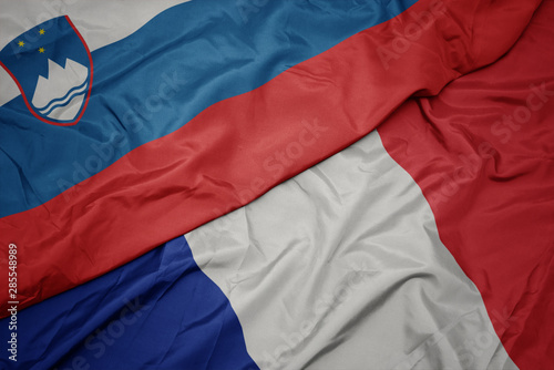 waving colorful flag of france and national flag of slovenia.