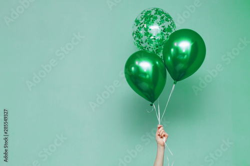 stylish birthday party or holidays with balloons. three  green balloons on the green background with copy space for text. Hand  holding three bright colorful balloons indoor.