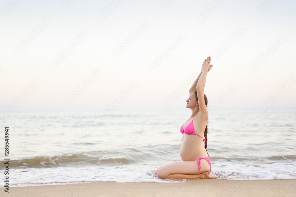 Young pregnant woman is practicing yoga sitting on the sea beach. Summer day Young pregnant woman is practicing yoga sitting on the sea beach. Summer day
