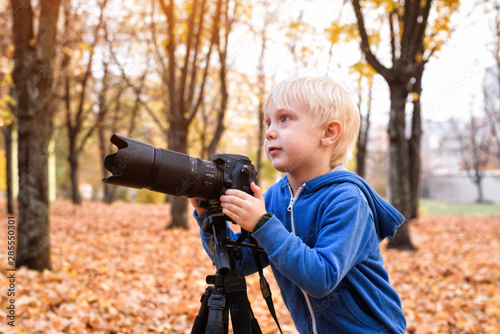 Little blond boy takes pictures on a SLR camera. Autumn Park