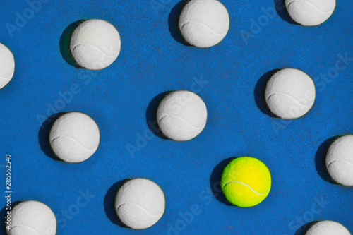 Creative composition made with yellow tennis ball and white balls on blue background.