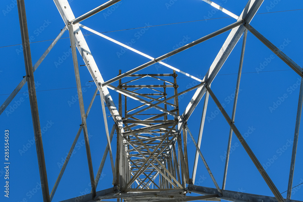 Supports high-voltage power lines against the blue sky. View from the bottom up