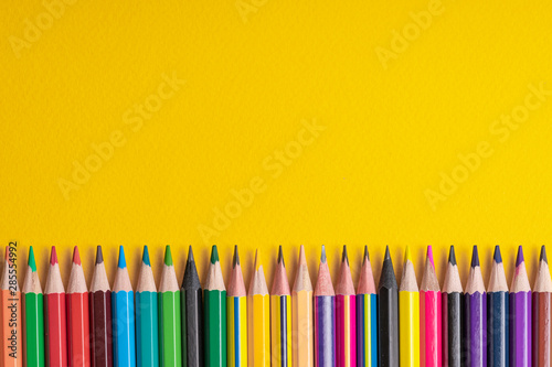 Many sharpened colored pencils laid out on a yellow background. Copyspace.