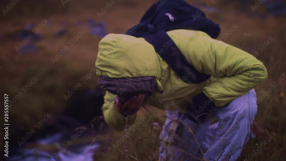 Man in yellow rain coat drinking from a mountain creek Man in yellow rain coat drinking from a mountain creek