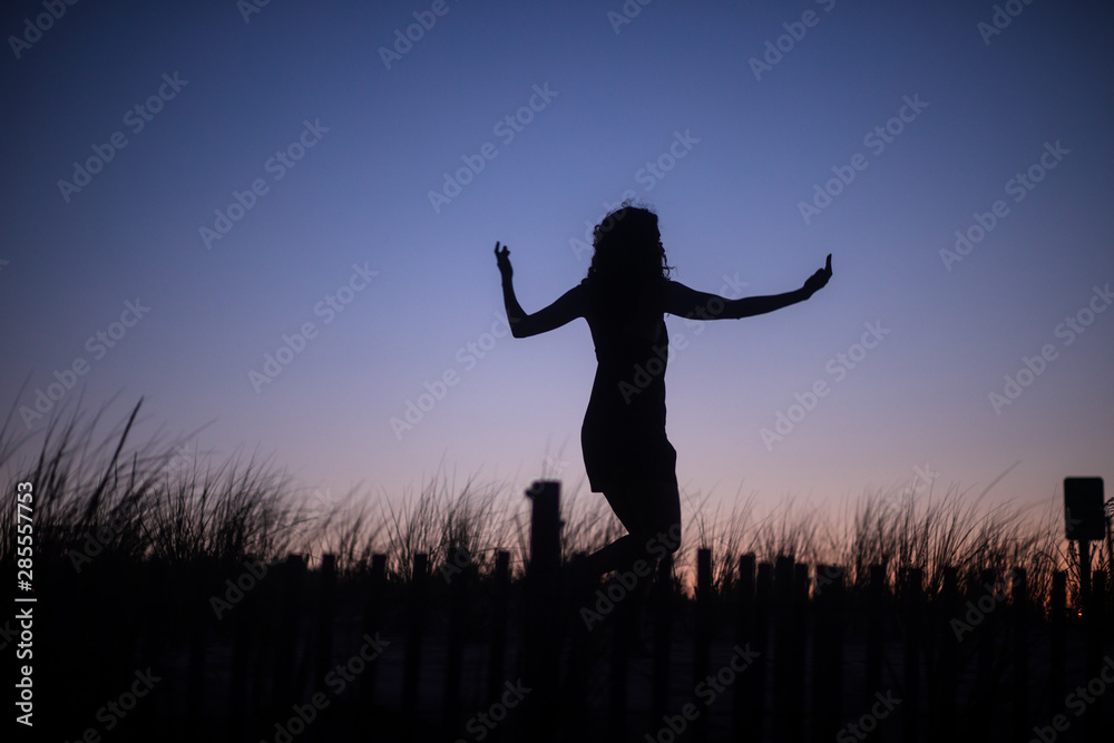 The silhouette of an unrecognizable woman practicing tai chi, yoga and minfulness at sunset