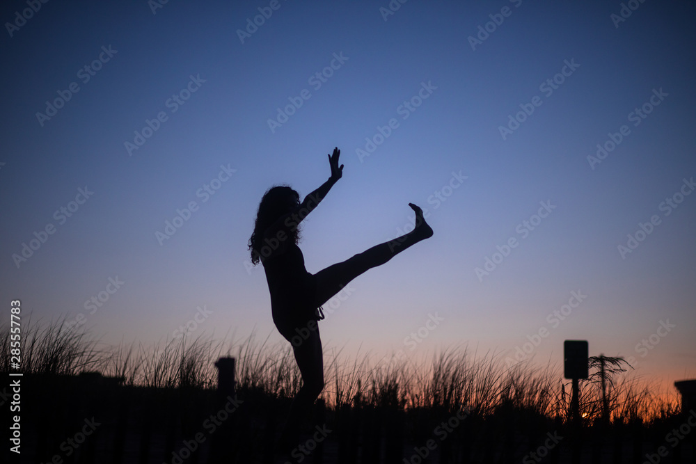 The silhouette of an unrecognizable woman practicing tai chi, yoga and minfulness at sunset