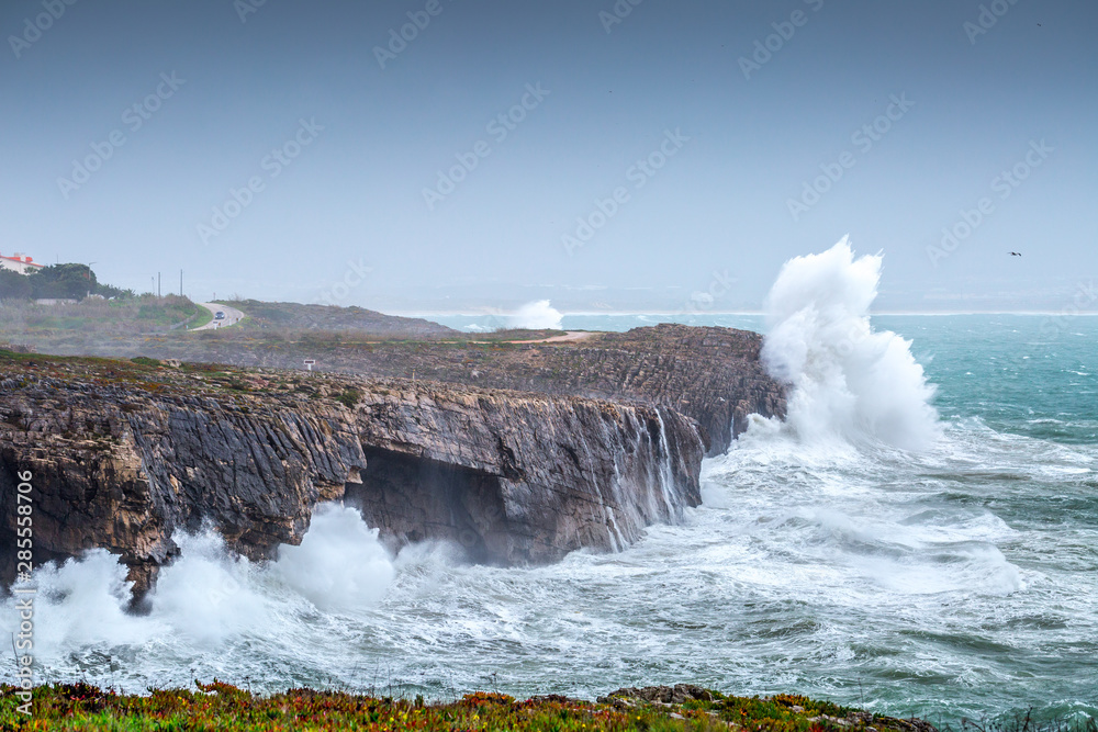 Obraz premium A huge ocean waves breaking on the coastal cliffs in at the cloudy stormy day. Breathtaking romantic seascape of ocean coastline. Peniche, Portugal.