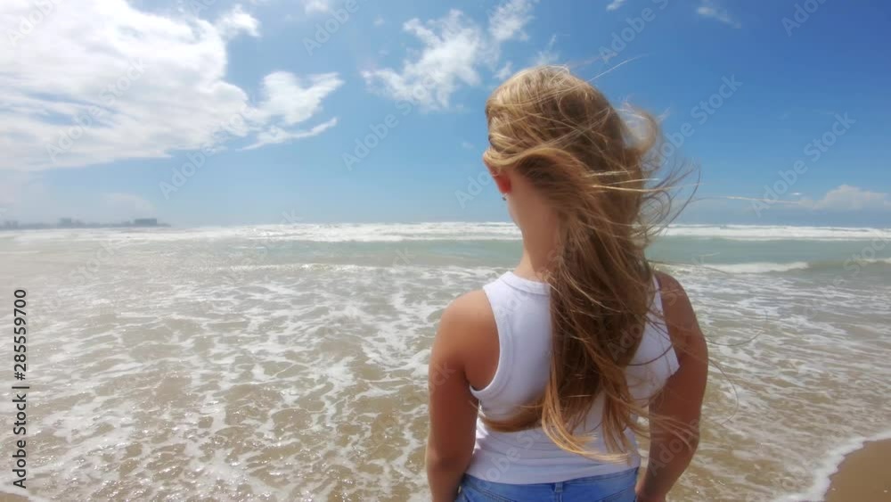 Girl looking at sea with wind in her hair. Beautiful blond hair develops in the wind and she is happy. Child by the sea with waves. Girl looking at sea with wind in her hair. Beautiful blond hair develops in the wind and she is happy. Child by the sea with waves.