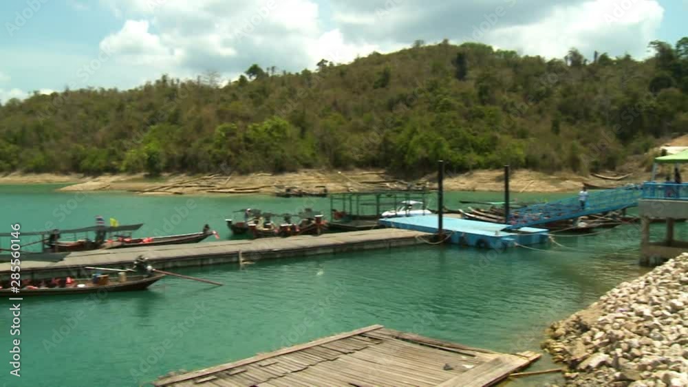 Handheld, medium wide shot of people walking up a dock ramp, camera pans to show docked boats and mountains. Handheld, medium wide shot of people walking up a dock ramp, camera pans to show docked boats and mountains.