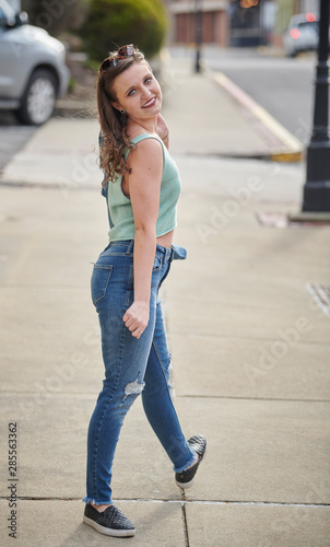 Stunning young female model walks on street in green blouse and blue jeans