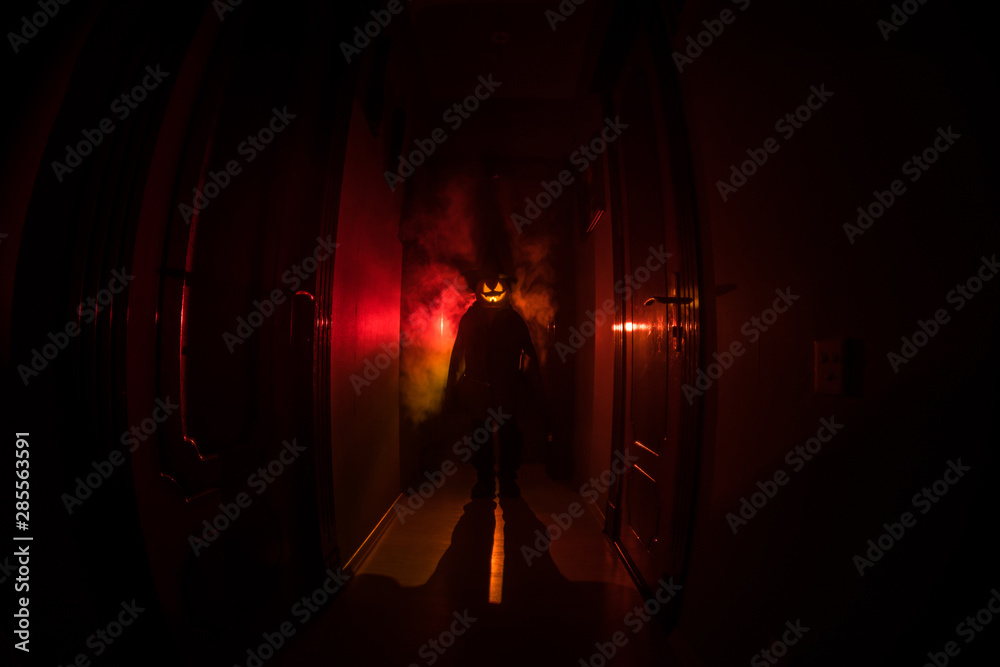 Halloween concept. Creepy silhouette in the dark corridor with pumpkin head. Toned light with fog on background. Selective focus